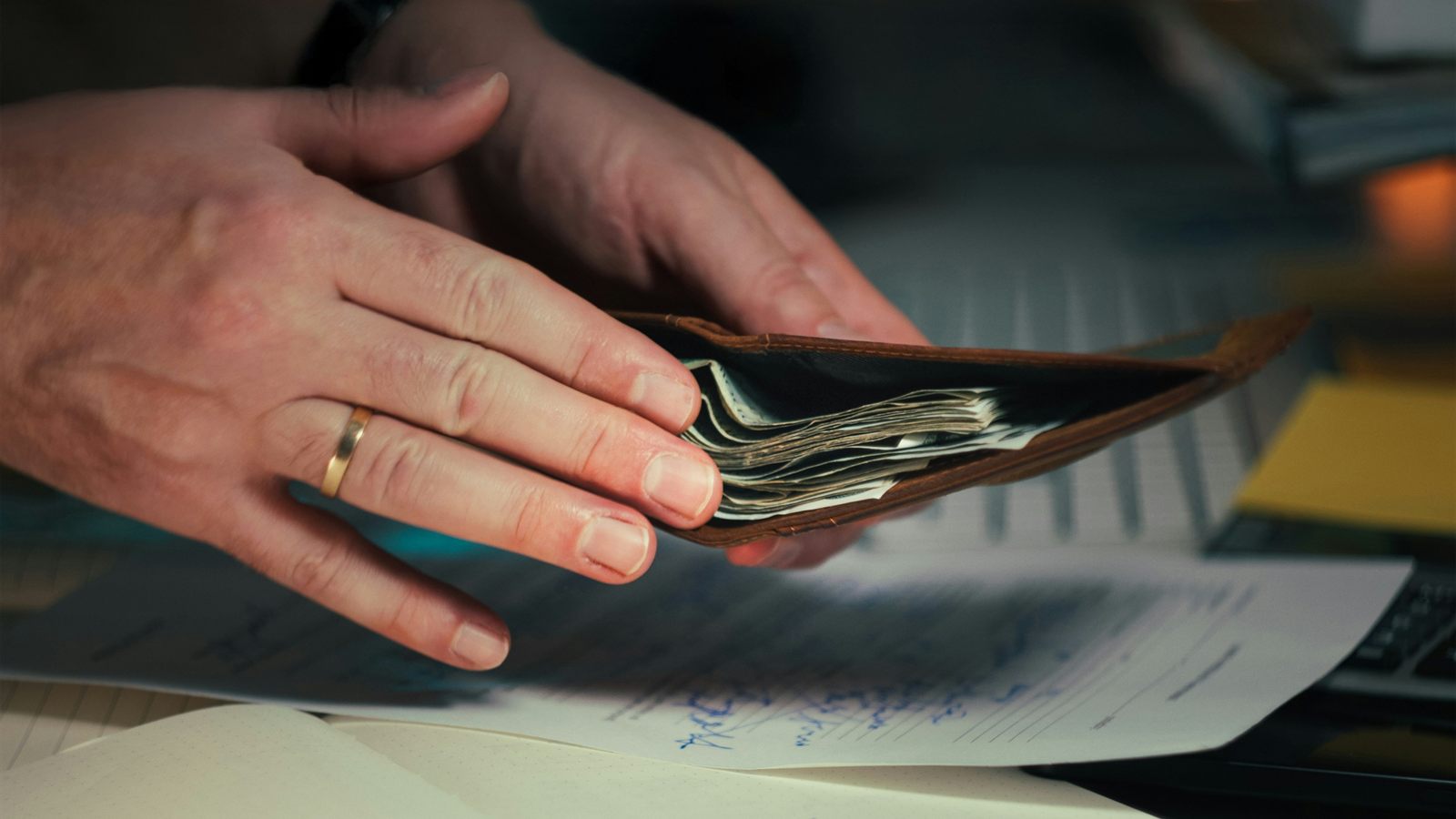 يدان تمسكان محفظة فيها أوراق نقدية فوق أوراق على مكتب