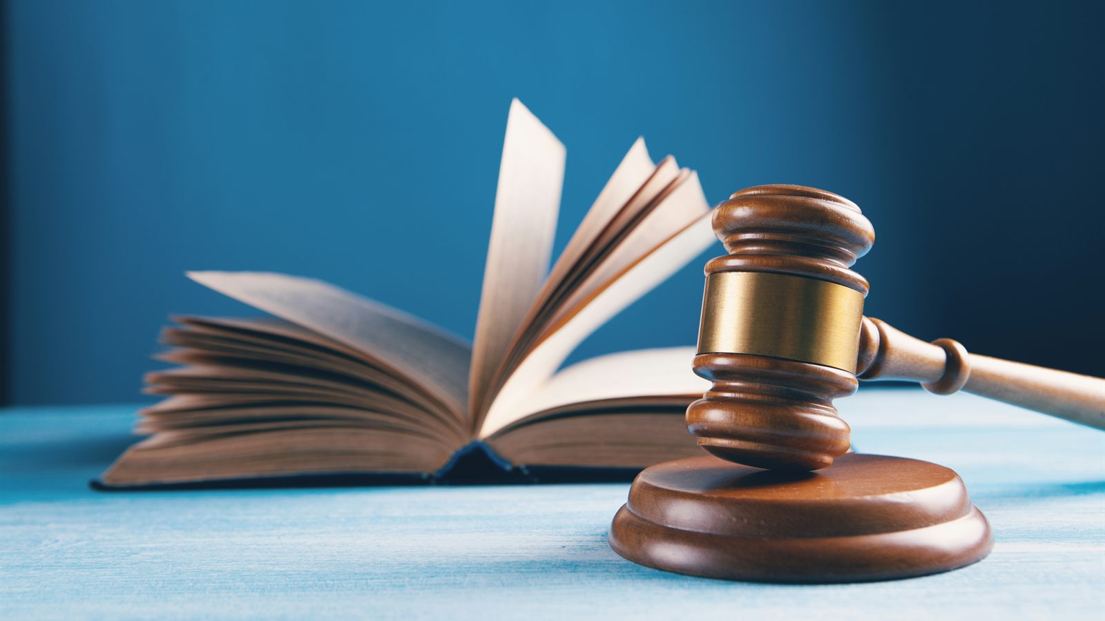 Mavi zemin önünde açık bir kitap ve ahşap hâkim tokmağı